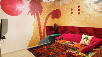 Una stanza con un divano rosso, un tappeto decorato, una televisione e un muro con un murale rosso e giallo.