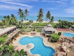 Ein Resort mit großem Pool, Palmen und Blick auf den Strand.