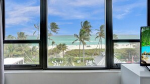 A room with large windows overlooking a beach with palm trees and a clear sky. - Resort beach condo w beach service /601 (Miami Beach)