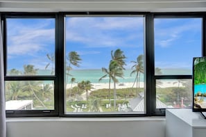Ein Zimmer mit großen Fenstern, die Blick auf einen Strand mit Palmen und einen klaren Himmel bieten.