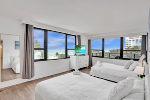 Ein modernes Hotelzimmer mit zwei Betten, einem Fernseher und großen Fenstern mit Blick auf den Strand.