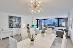 Ein modernes Hotelzimmer mit Essbereich, großem Fenster und Ausblick, einer Chandelieber und einem Wandbild.