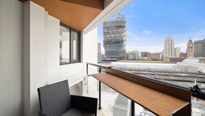 Un balcon offrant une vue sur le paysage urbain, notamment sur un bâtiment moderne en construction qui se distingue par son architecture.