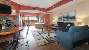 A living room with a pool table, a sofa, and a TV mounted on a stone wall. - River View Condo - Top Floor - Resort Pools - Pet Friendly! (Wisconsin Dells)