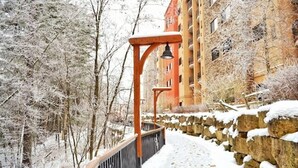 A snow-covered pathway leading to a building with a stone wall and a red structure with a bell. - River View Condo - Top Floor - Resort Pools - Pet Friendly! (Wisconsin Dells)