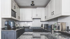Cocina moderna con gabinetes blancos, encimeras de granito y electrodomésticos de acero inoxidable.