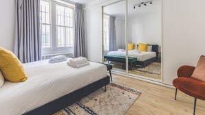Un dormitorio con cama, una silla, un espejo y un armario.