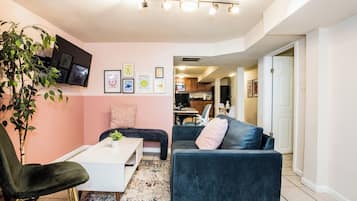 Un salon avec un canapé, un fauteuil, une table basse, un téléviseur et une plante.