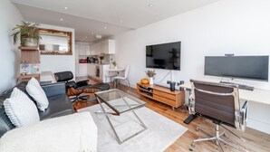 Una sala de estar moderna con sofá, mesa de centro, televisor y un comedor con cocina al fondo.