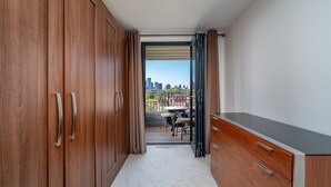 Pasillo que conduce a un balcón con vistas a la ciudad, armario de madera y una pequeña mesa con sillas.