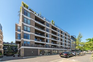 Ein mehrstöckiges Wohngebäude mit Balkonen, einem überdachten Eingang und blauem Himmel.