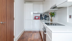 Cocina compacta con armarios blancos, un microondas rojo, una cafetera y un florero con hojas verdes.