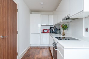 Eine kleine Küche mit weißen Schränken, einer roten Mikrowelle, einer Kaffeemaschine und einer Vase mit grünen Blättern.