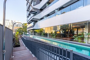 Un bâtiment moderne doté d’une piscine sur le toit, entouré d’une terrasse en bois et de rampes en métal.