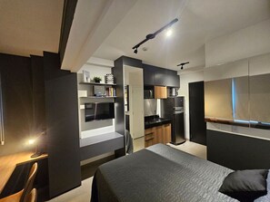 A compact hotel room with a bed, a desk, a kitchenette, and a TV. - Studio Moderno - Oscar Freire (São Paulo)
