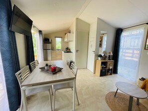 A compact kitchen with a microwave, stove, and cabinets, a dining area with a table and chairs, and a small round table with a rug. - 4-person mobile home in a family campsite in the mountains  (Saillagouse)