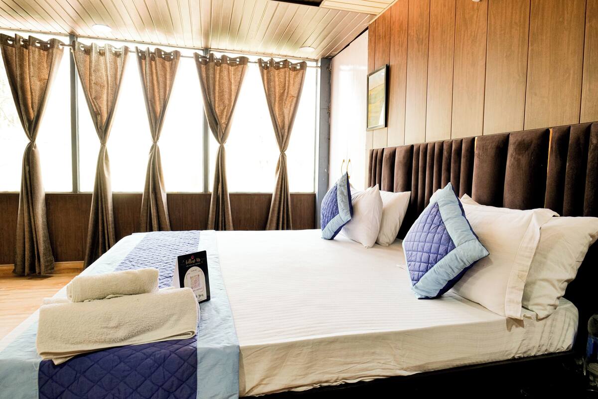 A hotel room with a large bed, curtains, a headboard, and a framed picture on the wall.