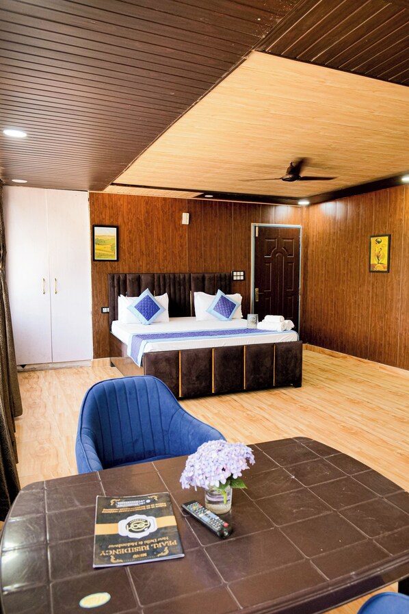 A hotel room with a bed, a desk with a remote control, and a vase with flowers. - Aarohan - By Shivaneel Hospitality (Dhari)