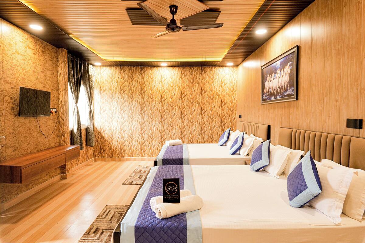 A hotel room with two beds, a ceiling fan, a mounted TV, and a painting on the wall.