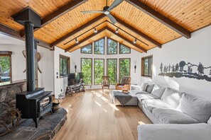 Ein geräumiges Wohnzimmer mit Kamin aus Stein, einem großen grauen Sofa und einem Fernseher.