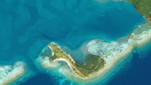 Vue aérienne d’une île côtière, avec ses eaux cristallines, ses plages de sable et un petit village.