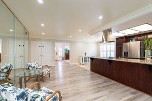 A spacious living area with a glass coffee table, floral armchairs, a kitchen with dark wood cabinets, and a large window. - Spacious 3BR San Diego Home w/ Parking & AC Modern (San Diego)