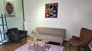 Ein Wohnzimmer mit einer Couch, Sesseln, einem Couchtisch, einem Bücherregal und einem Poster an der Wand.