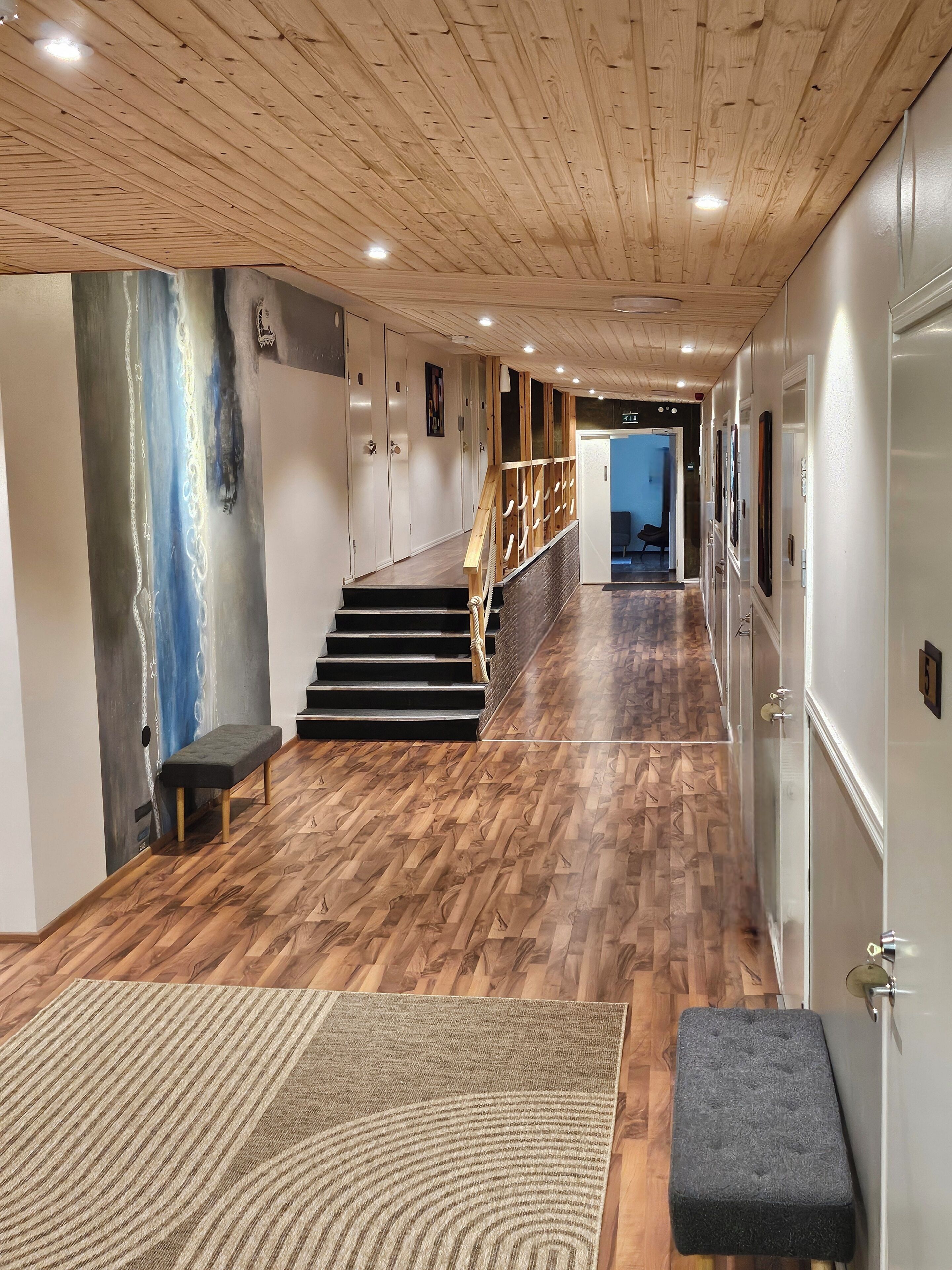 Un pasillo con piso de madera, una escalera y un banco.