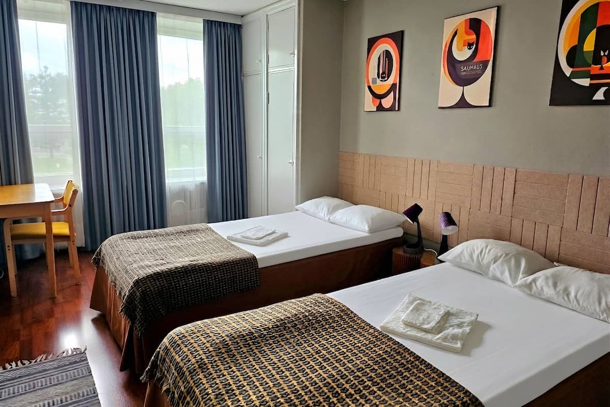 Una habitación de hotel con dos camas, un escritorio y una ventana con cortinas.