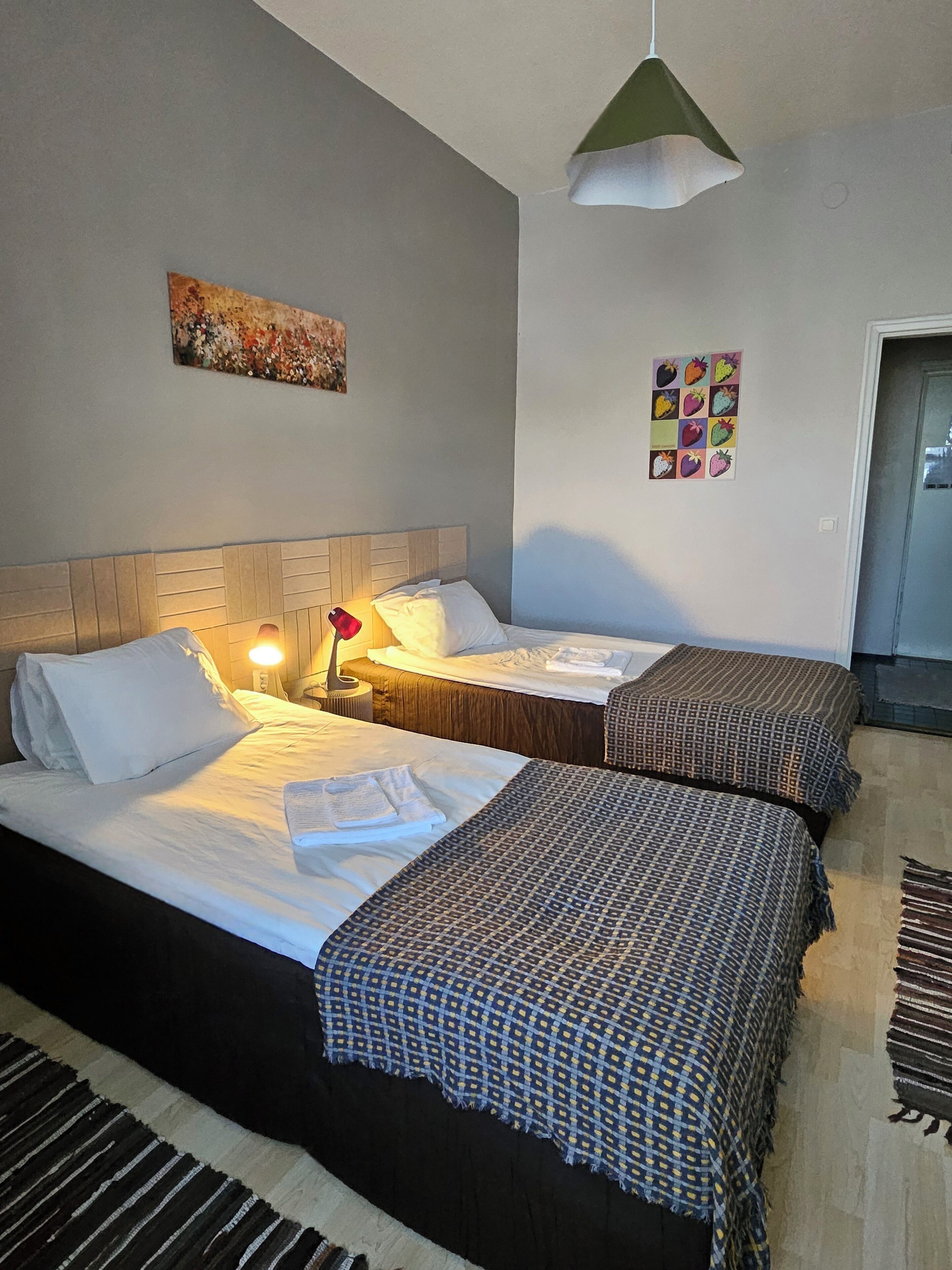 Hotellihuone, jossa on kaksi sänkyä, yöpöytä, lamppu ja taulu seinällä.
