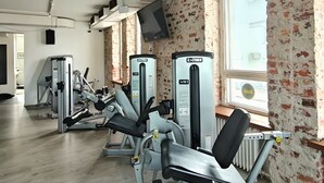 Un gimnasio con diversas máquinas de ejercicio, un ventanal grande y una pared de ladrillo.