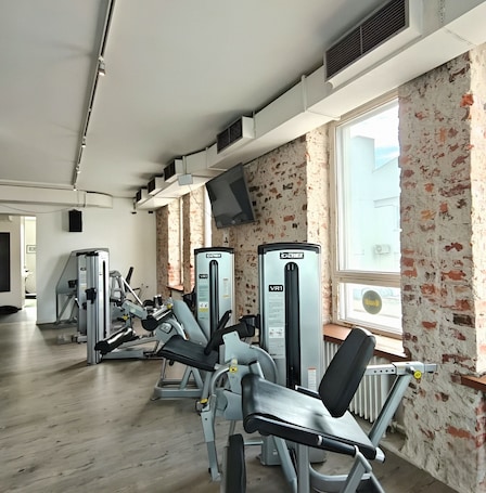 A gym with various exercise machines, a large window, and a brick wall.. Hotelli Suonenjoki
