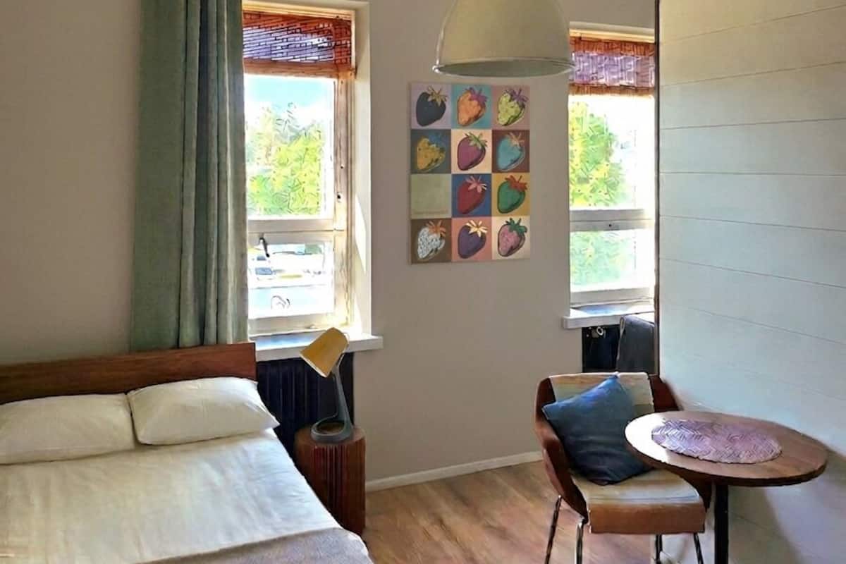 Una habitación con cama, una mesa de comedor, una silla, una lámpara y un ventanal con cortinas.
