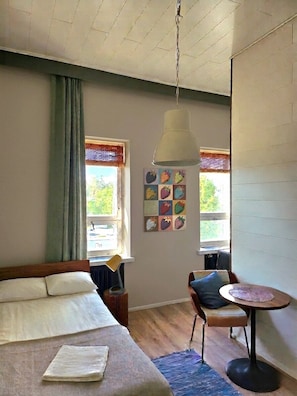 A room with a bed, a dining table, a chair, a lamp, and a window with curtains.