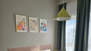 Cama doble con ropa blanca, cabecero y mesita de noche con lámpara. Tres obras de arte decoran la pared sobre la cama.