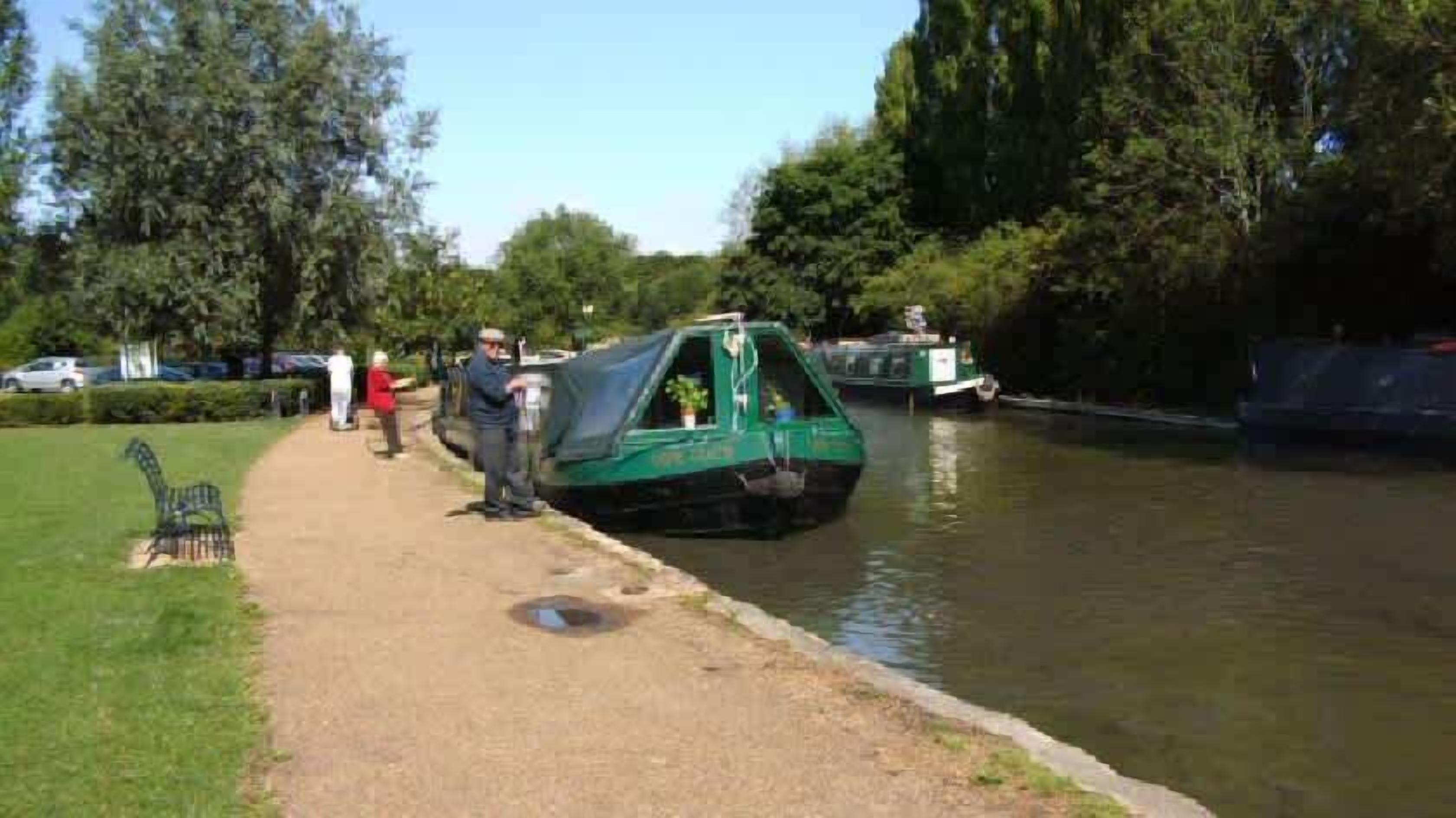 A narrow waterway with a green boat, a paved walkway, and people in the background.
