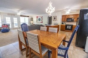 A dining area with a wooden table and chairs, a chandelier, and a kitchen with wooden cabinets and appliances.