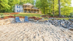 A two-story house with a covered porch and a landscaped yard with a sandy area and seating.