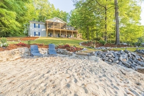 A two-story house with a covered porch and a landscaped yard with a sandy area and seating.
