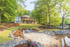 A two-story house with a covered porch, surrounded by a landscaped garden with a pond, rocks, and flowers.