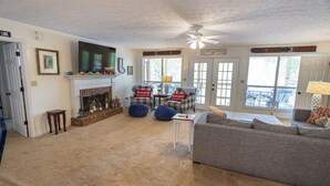 A living room with a fireplace, a ceiling fan, and a view of the outside.