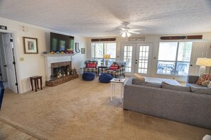 A living room with a fireplace, a ceiling fan, and a view of the outside.