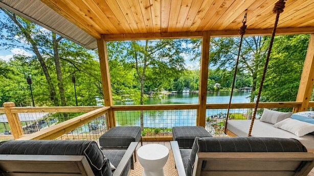 A wooden deck with outdoor seating, a swing, and a view of a lake.