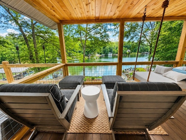 A wooden deck with outdoor seating, a swing, and a view of a lake.