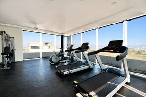 Ein Fitnessstudio mit Laufbändern, Crosstrainern und Kraftgeräten, großen Fenstern und Blick auf die Stadt.