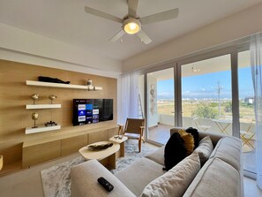 Ein modernes Wohnzimmer mit Fernseher, Deckenventilator, Sofa, Couchtisch und einem Balkon mit Blick.