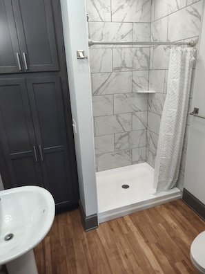 A bathroom with a shower, a sink, and dark cabinets.