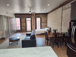 A spacious room with a bed, a dining table, chairs, a sofa, and a ceiling fan.