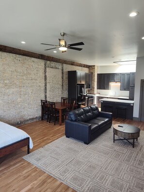 A modern living space with a dining area, kitchen, and a large black leather sofa.
