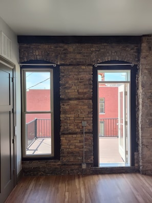 A room with two large windows, a brick wall, and a wooden floor.